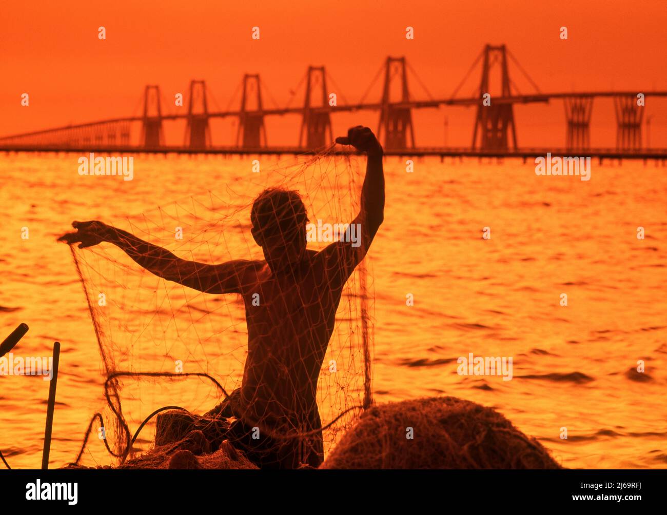 Silhouette of a fisherman with the Rafael Urdaneta bridge in the background at sunrise, Zulia State, Venezuela Stock Photo
