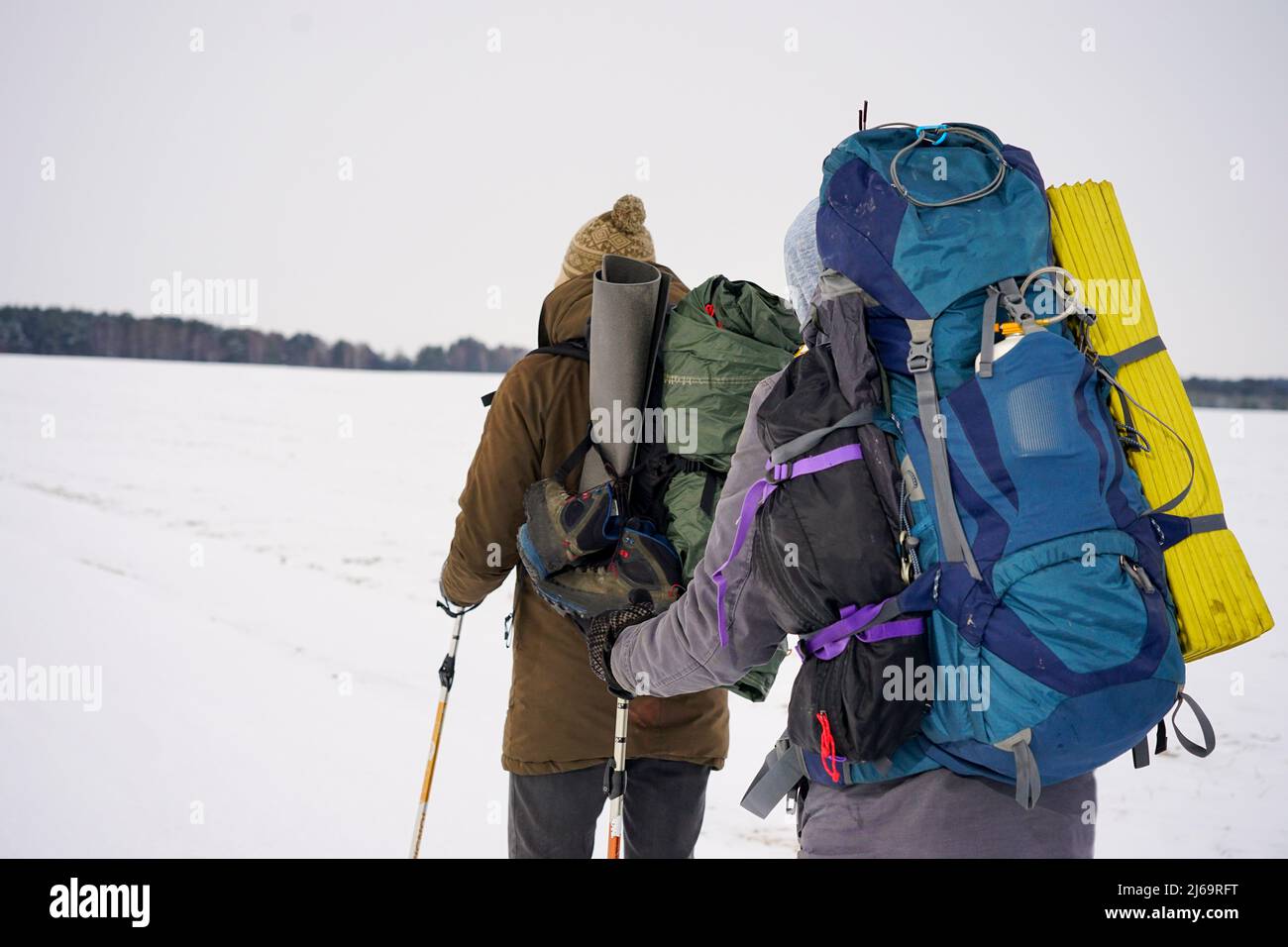 Two guys walk through loose snow during a winter expedition. They carry large backpacks, warm jackets. They hold trekking sticks in their hands. Stock Photo