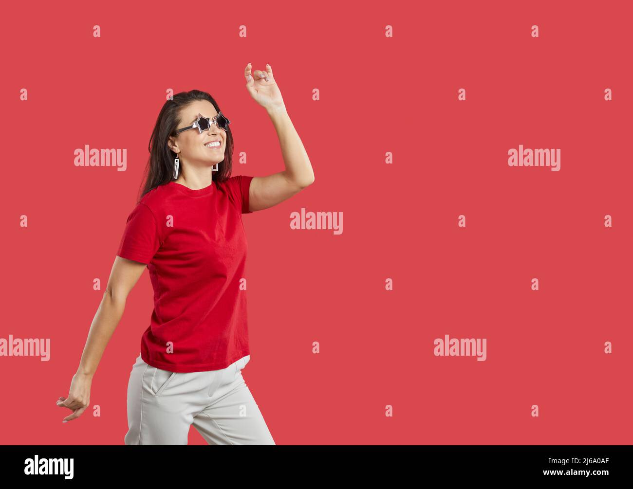 Cheerful positive woman in funny glasses with stars isolated on vivid red background. Stock Photo