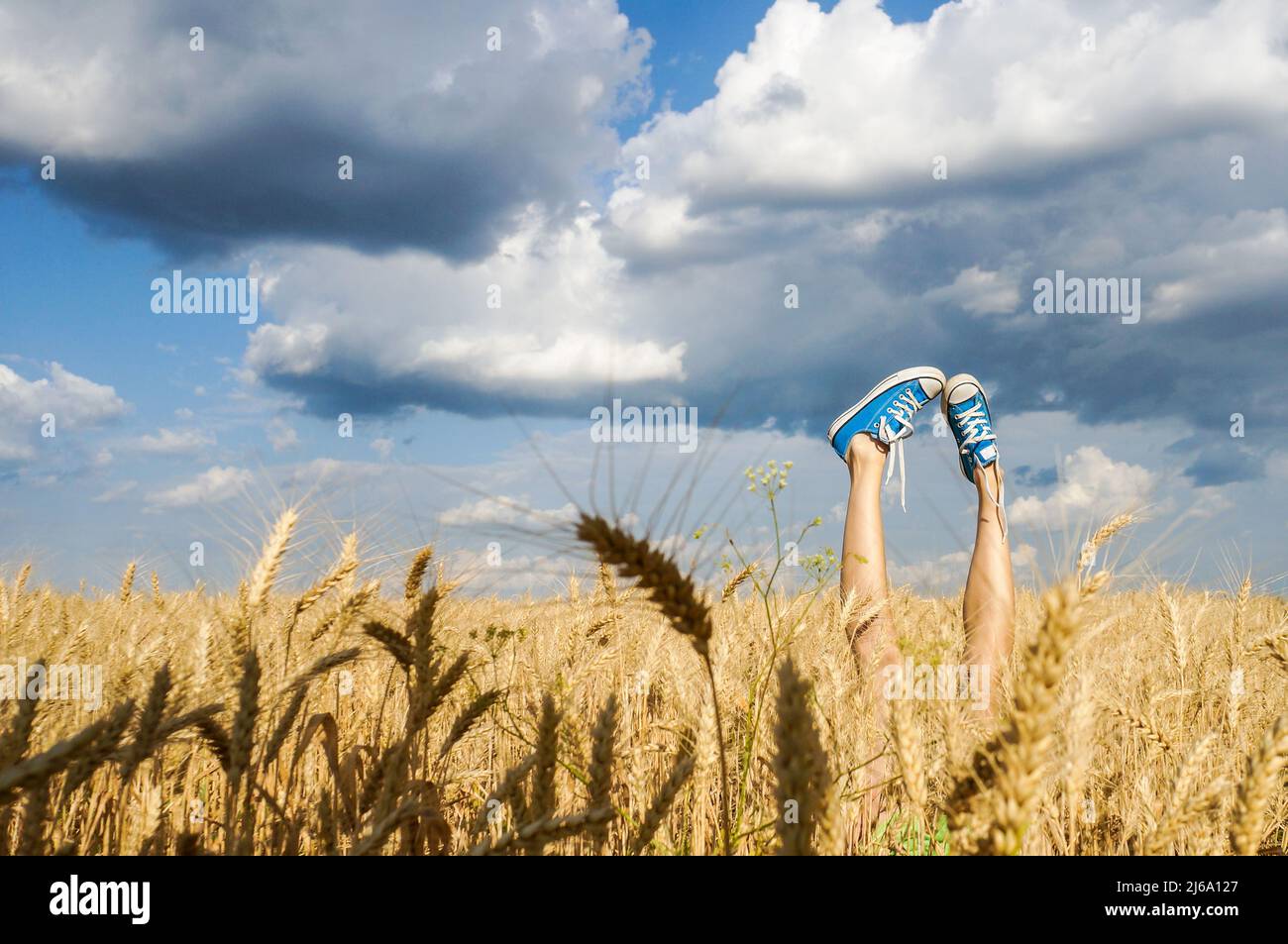 female legs wearing sneakers over field and cloudy sky Stock Photo