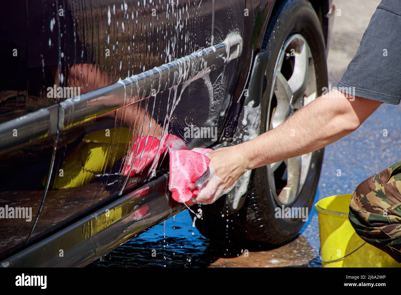 Man washes car wheel. Male hand holds pink sponge with soapy foam for
