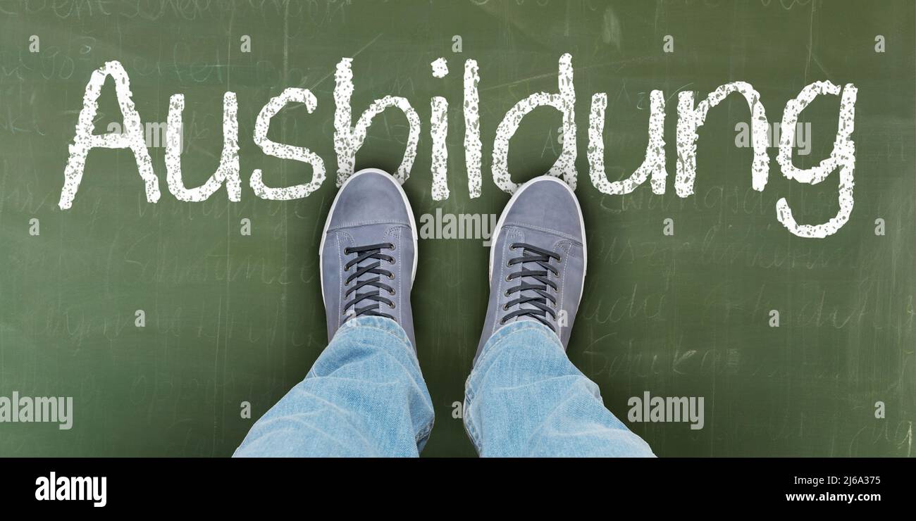 A person stands on a school blackboard with the word "education" ("Ausbildung" in German) Stock Photo