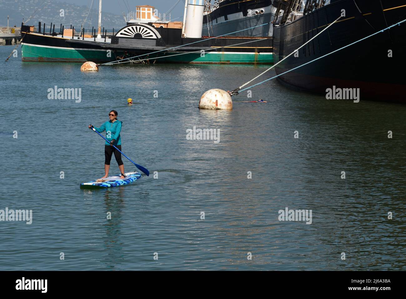 A woman enjoys riding a stand up paddle board in San Francisco Bay offshore from the Fisherman's Wharf district of San Francisco, California. Stock Photo