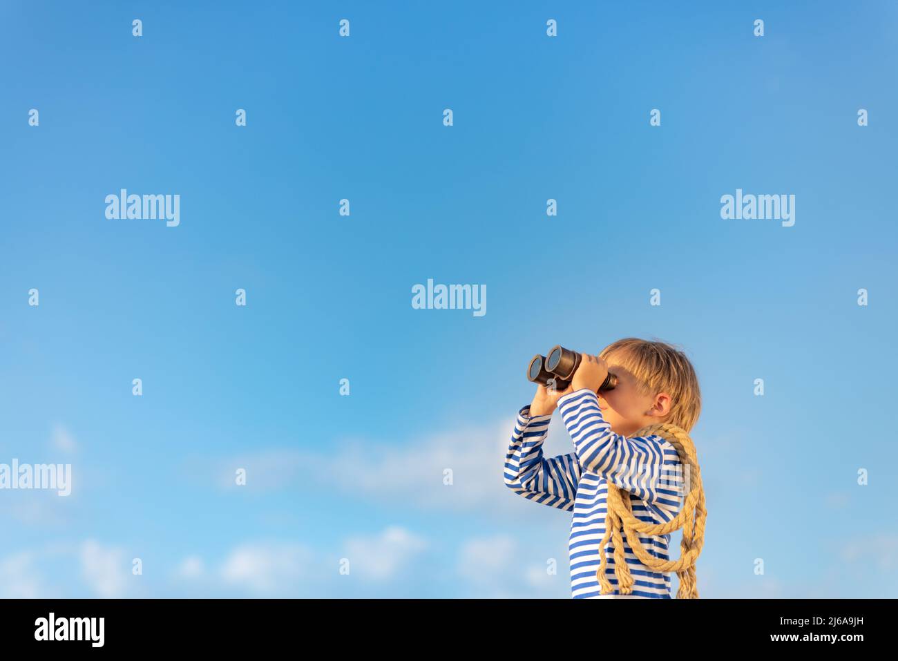Happy child looking through vintage binoculars against blue sky. Kid having fun in summer. Imagination and freedom concept. Stock Photo