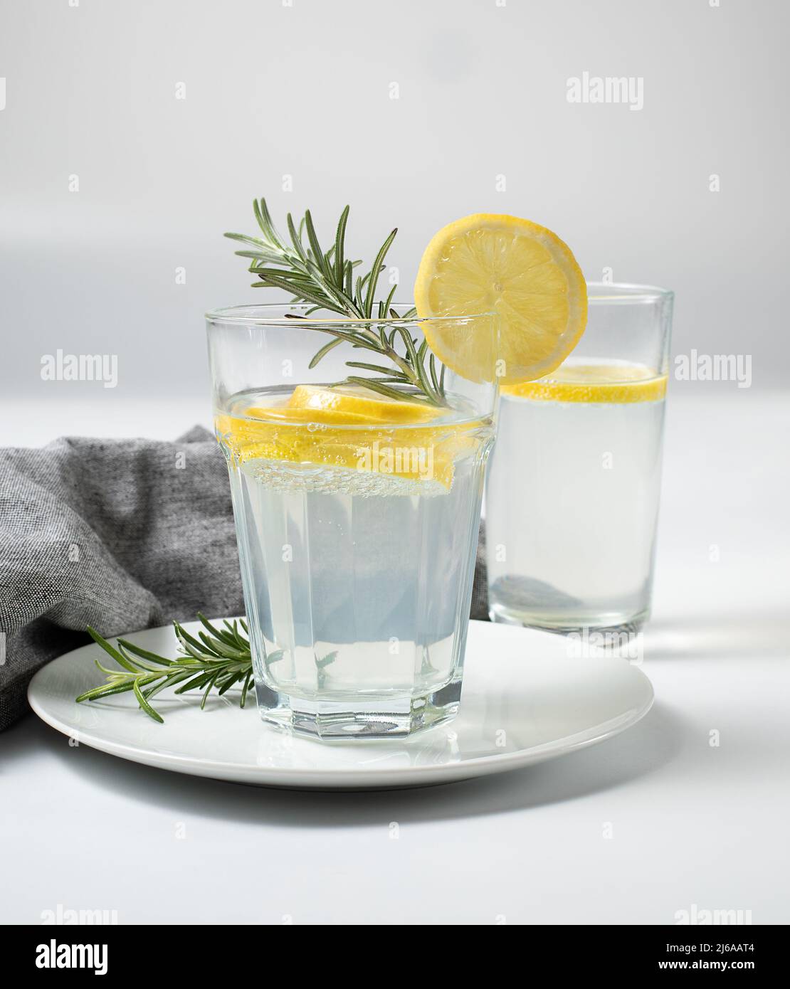 Two glasses with fresh lemon water or homemade lemonade with rosemary on white background, textile, stock photo, concept Stock Photo