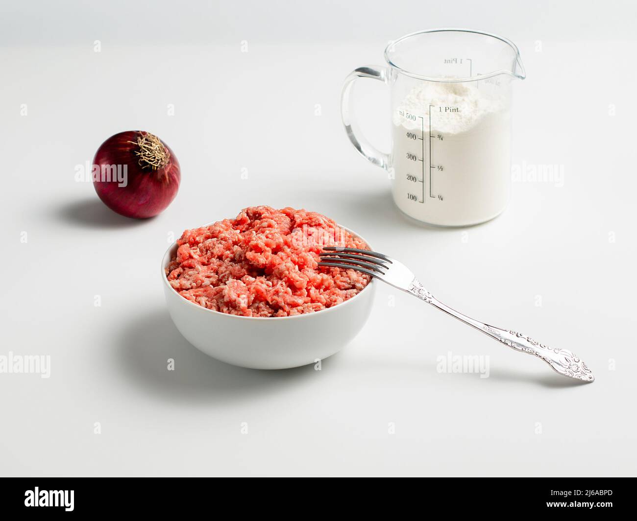 Plate with fresh ground beef and fork, red onion, measuring cup with