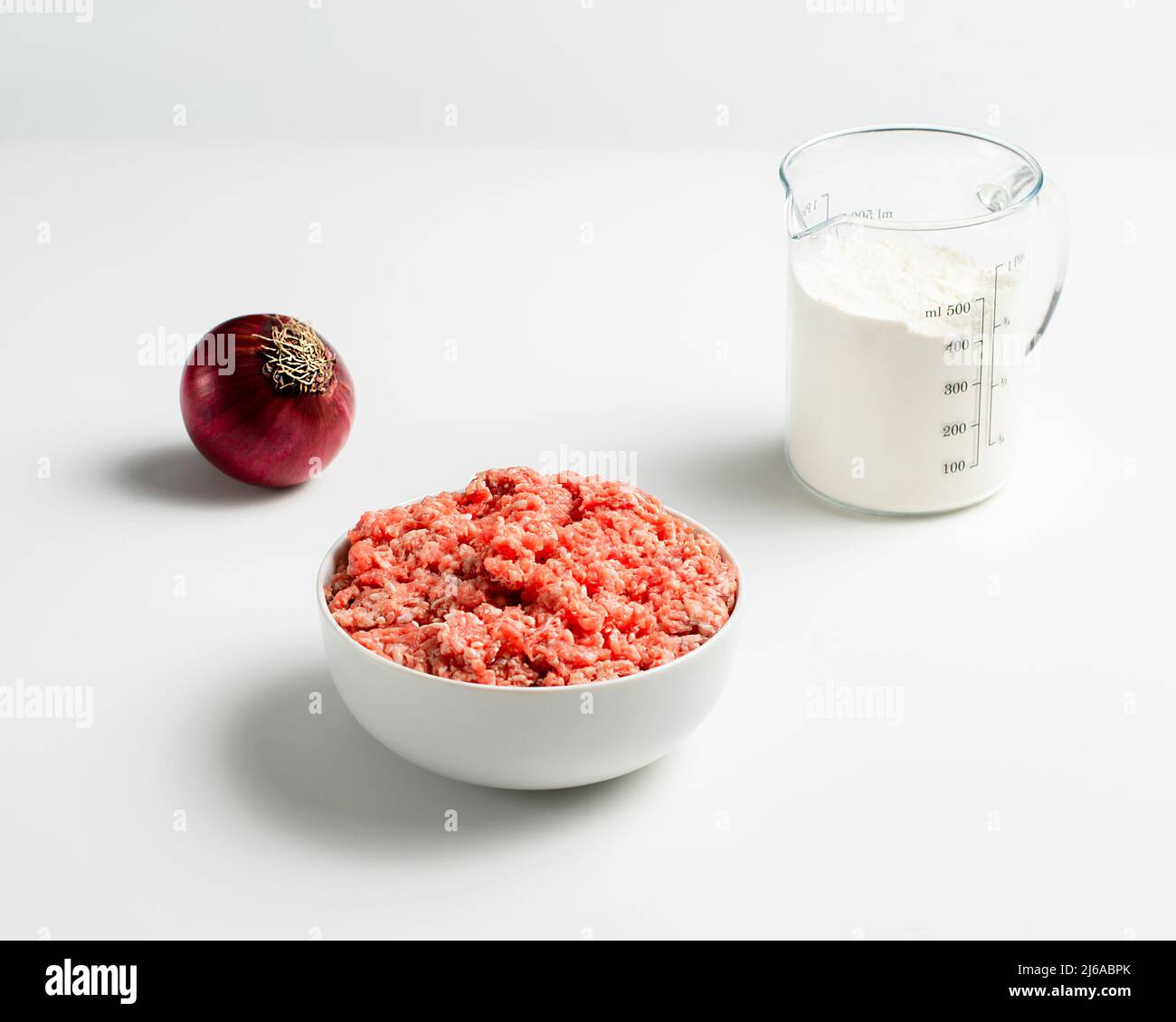 Plate with fresh ground beef, red onion, measuring cup with flour on a