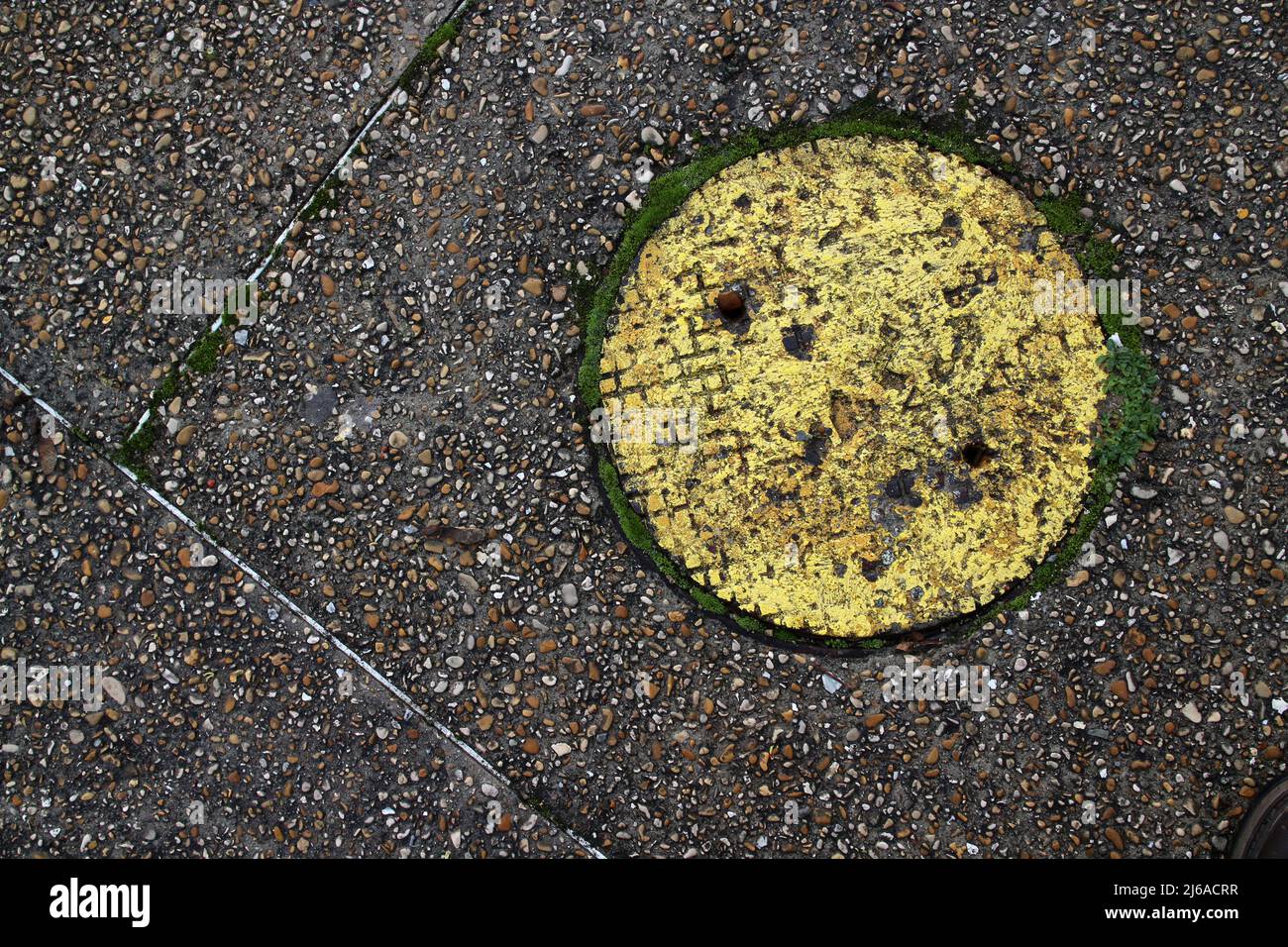 Yellow-painted manhole surrounded by grass on old tarmac Stock Photo