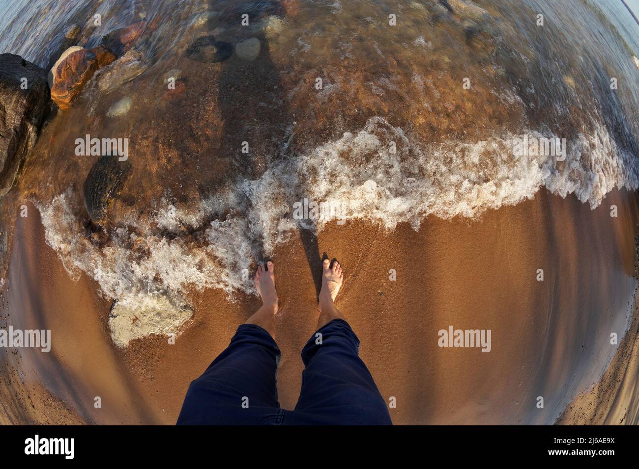 First Person Fisheye Perspective of Man's Feet in Shallow Water with Waves Rolling into Sandy Beach Stock Photo