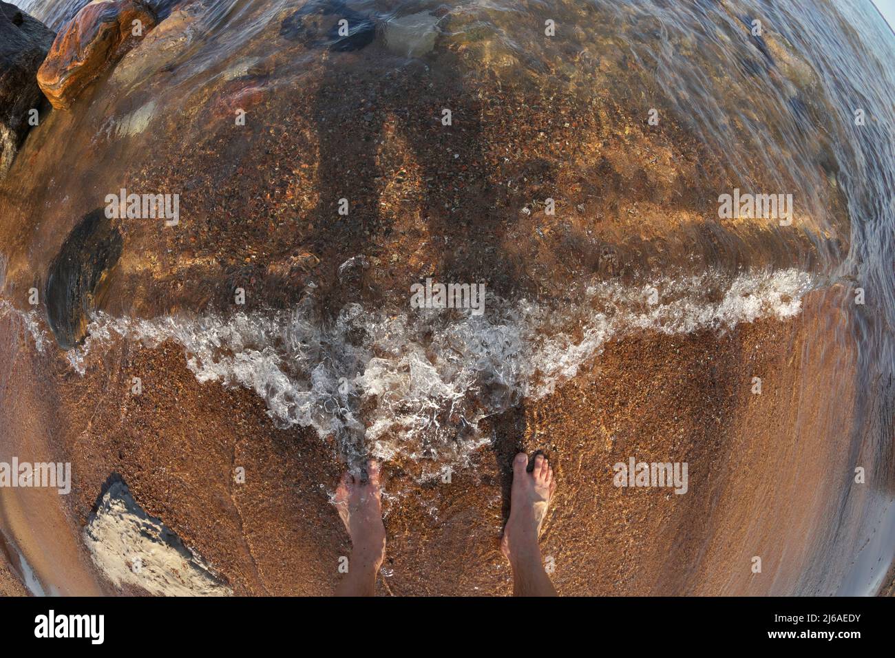 First Person Fisheye Perspective of Man's Feet in Shallow Water with Waves Rolling into Sandy Beach Stock Photo