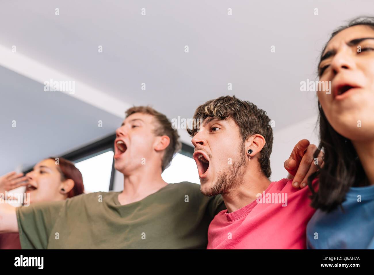 friends screaming with joy watching e-sports on TV after their team's victory. group of young people partying at home. Stock Photo