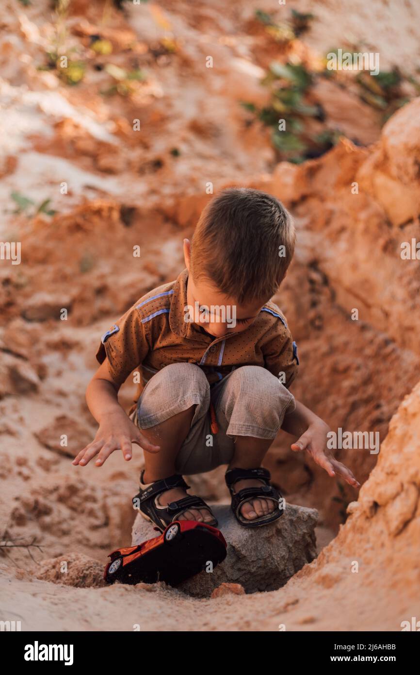 A little boy sits in the sand playing with a small car Stock Photo