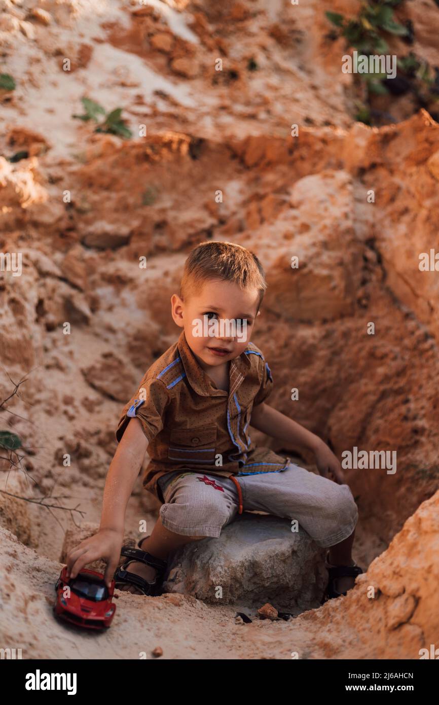 A little boy sits in the sand playing with a small car Stock Photo