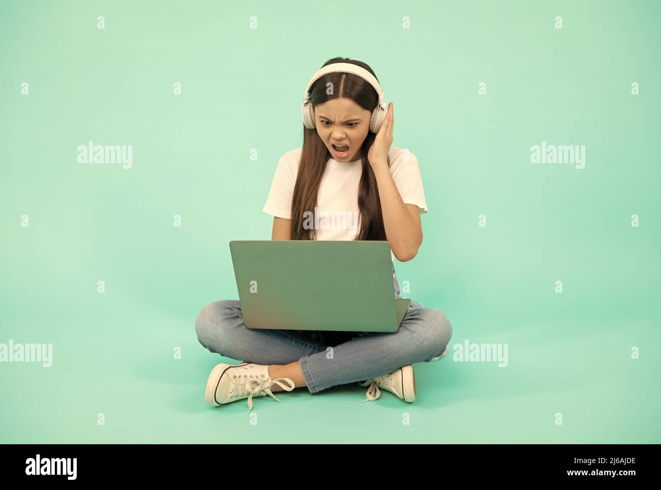 shocked kid girl influencer use computer for video call or listen webinar in headphones, blogging. Stock Photo