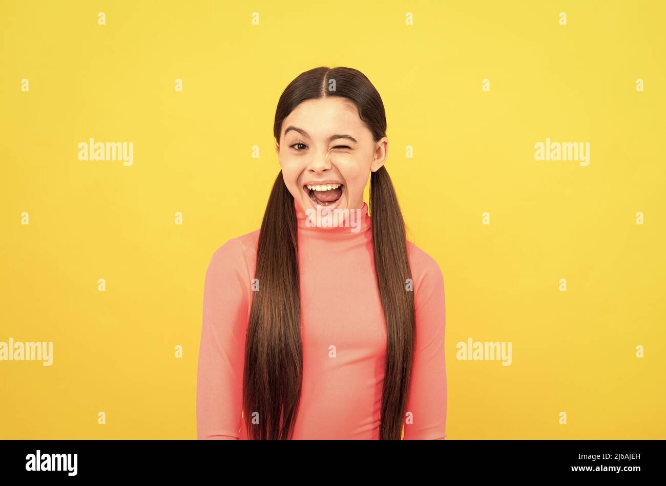 winking child with long hair on yellow background, emotions Stock Photo