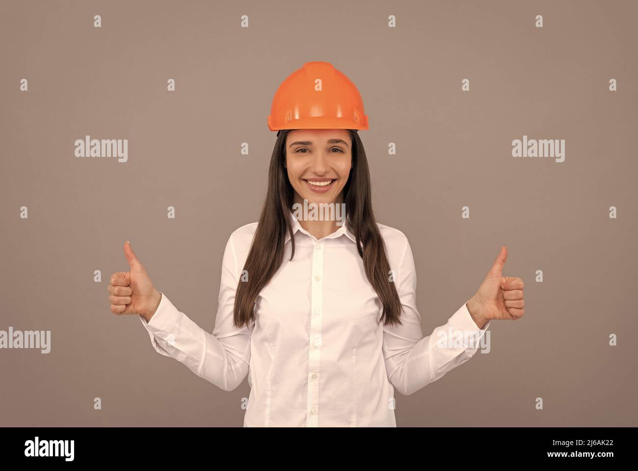 happy woman in protective helmet and white shirt showing thumb up gesture, good result Stock Photo