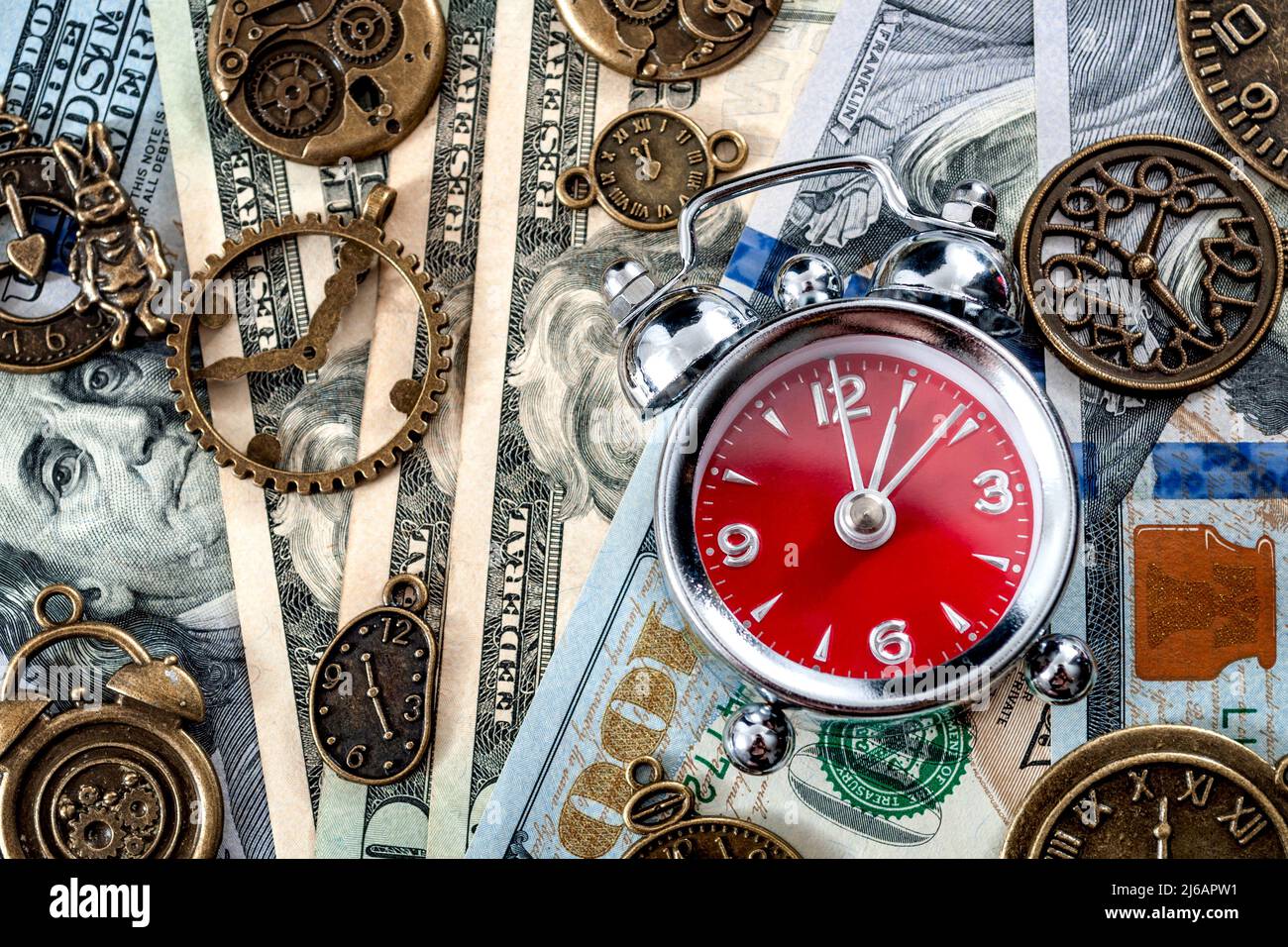 Time is money concept with flat lay of alarm clock on dollar bill or notes and surrounded by metal clocks Stock Photo