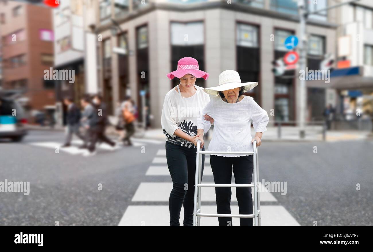 Daughter take care elderly woman walking across the street in downtown Stock Photo