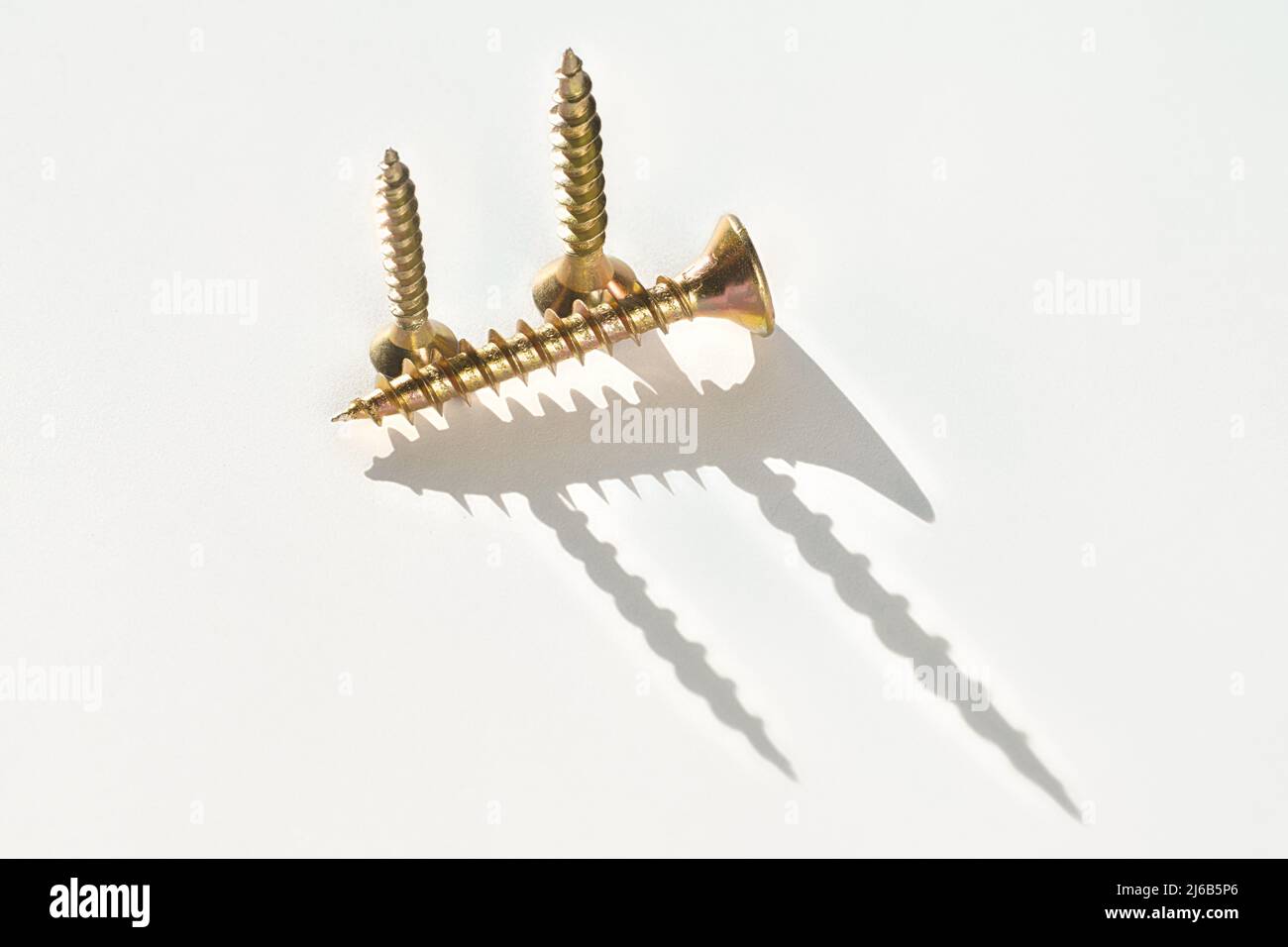 Three golden screws on a white background with long shadows. Close up of screws with selective focus Stock Photo