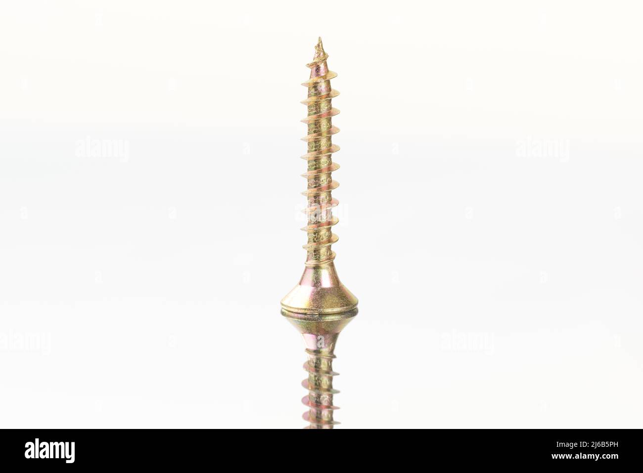 Gold colored screw close up standing on a mirror surface with reflection. Isolated on white, clipping path included Stock Photo