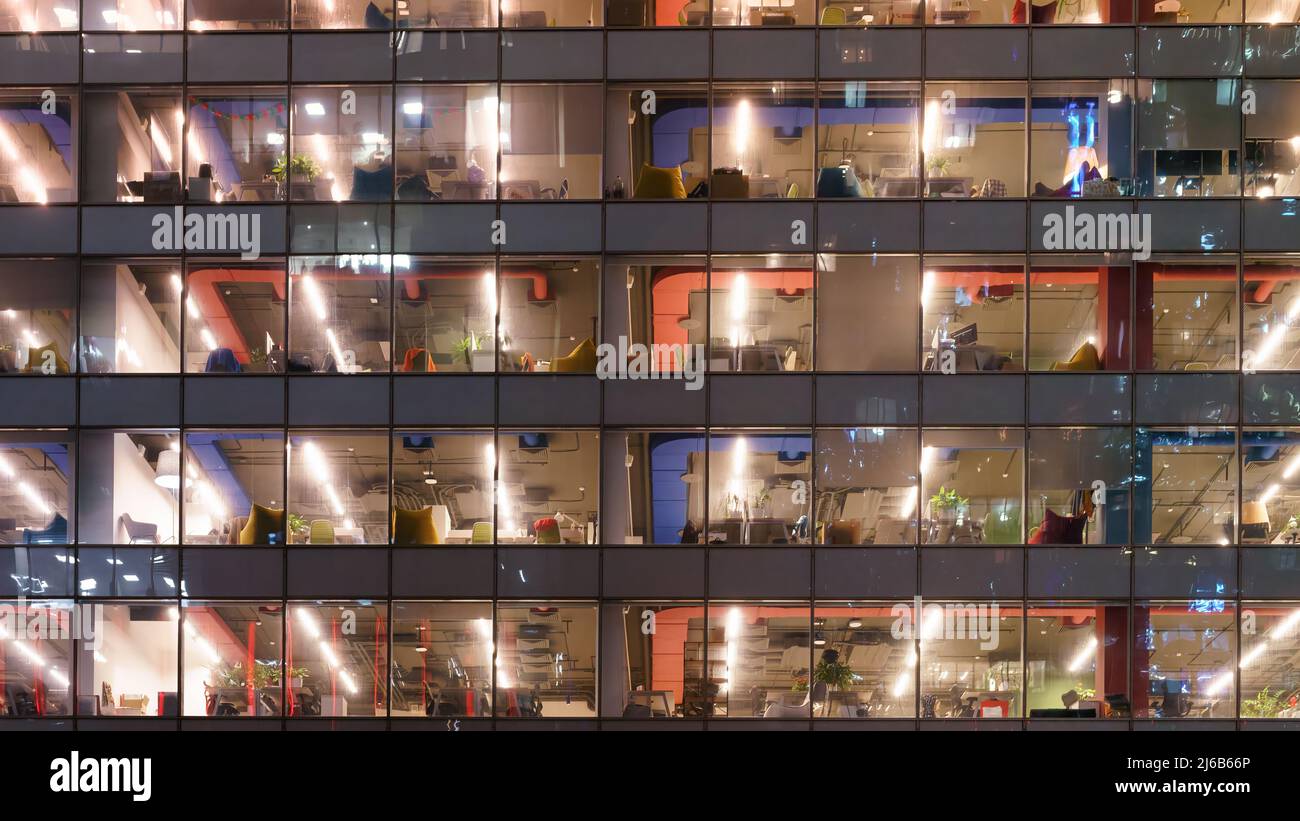 Glass wall of an office building with depersonalized interiors behind glass. Night shoot Stock Photo