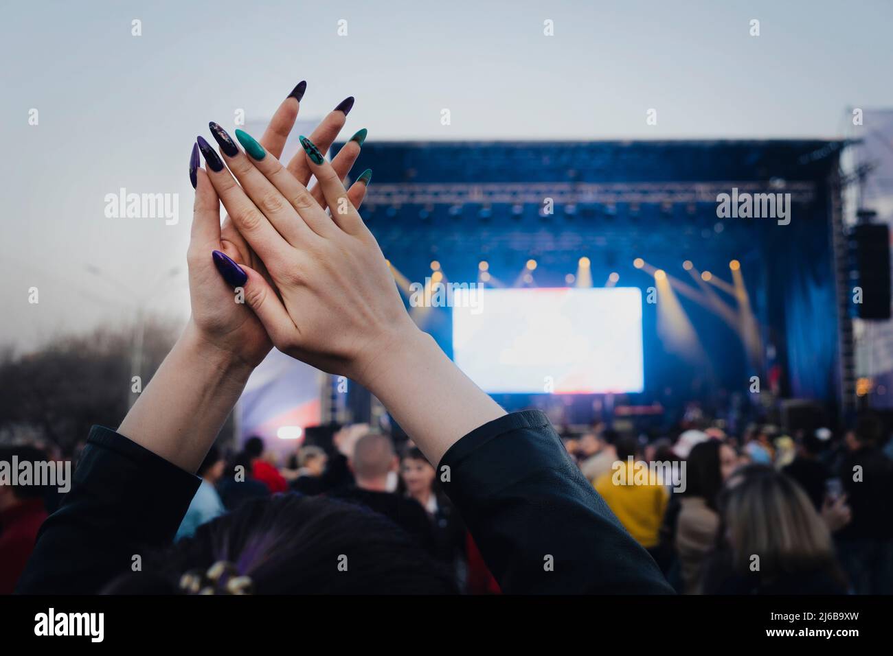 woman claps his hands at a musical concert in a crowd of people. clapping crowd at singer's concert. smoke, applause and hands in soft focus, abstract Stock Photo