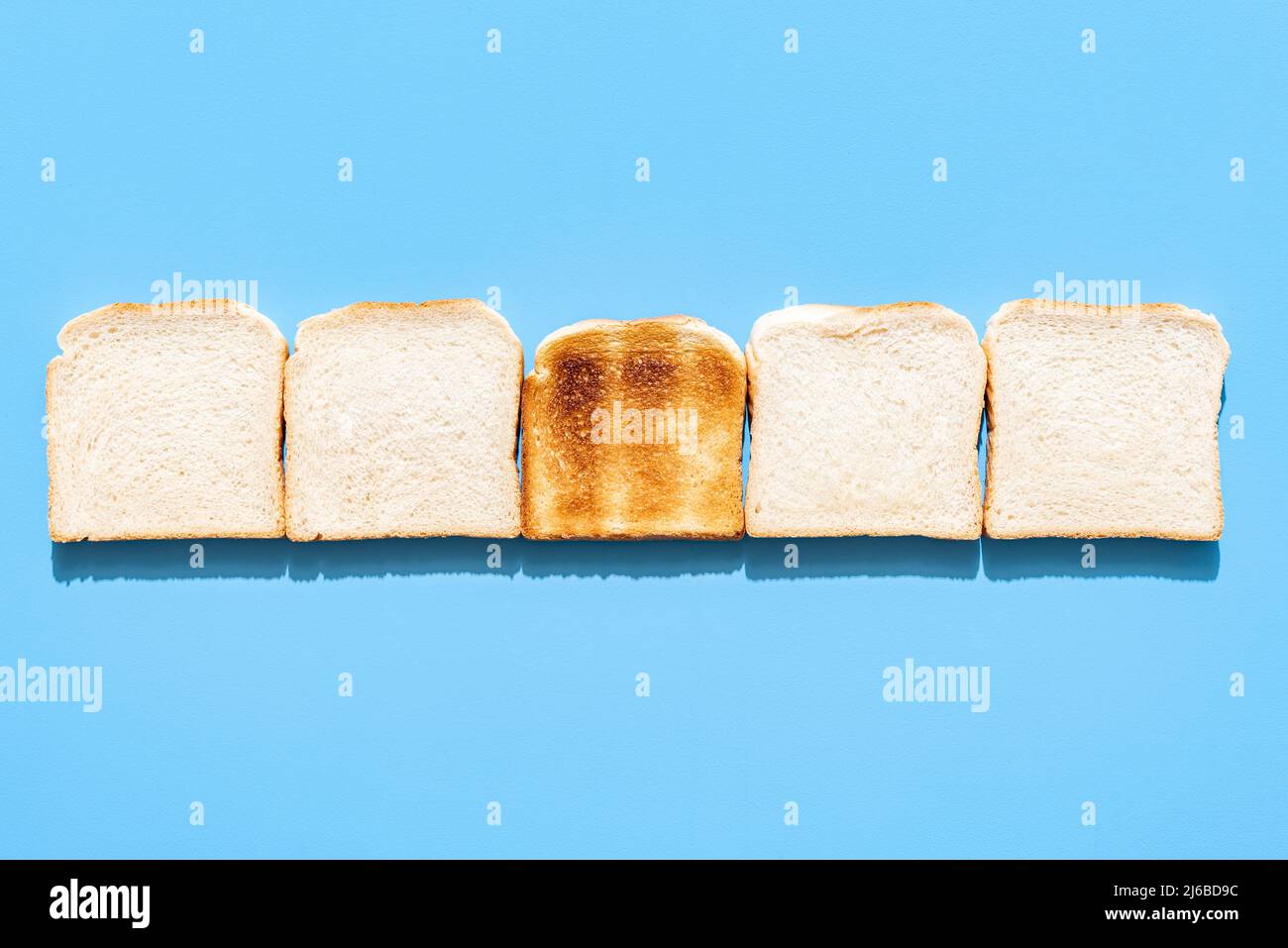 Above view with slices of bread aligned on a blue table. A single piece