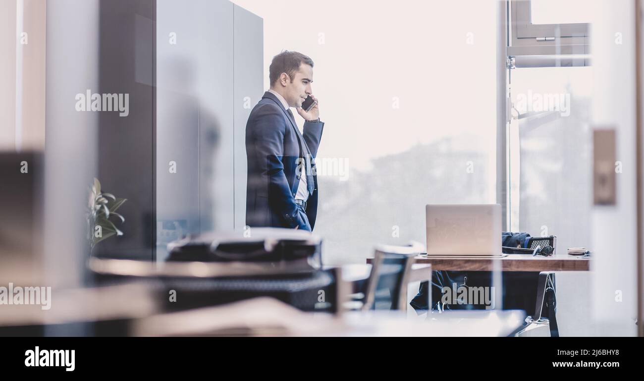 Businessman talking on a mobile phone while looking through window. Stock Photo