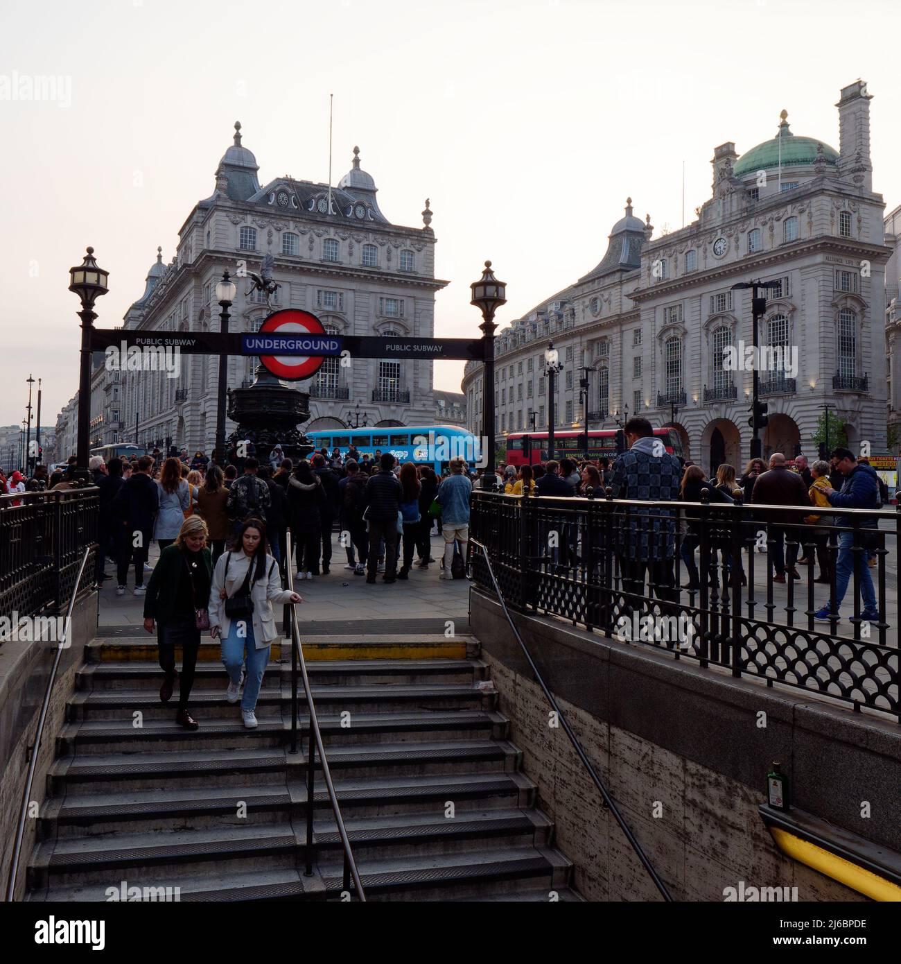 London, Greater London, England, April 23 2022: Piccadilly Circus as seen from the tube station as crowds gather to watch a street act and a red and b Stock Photo
