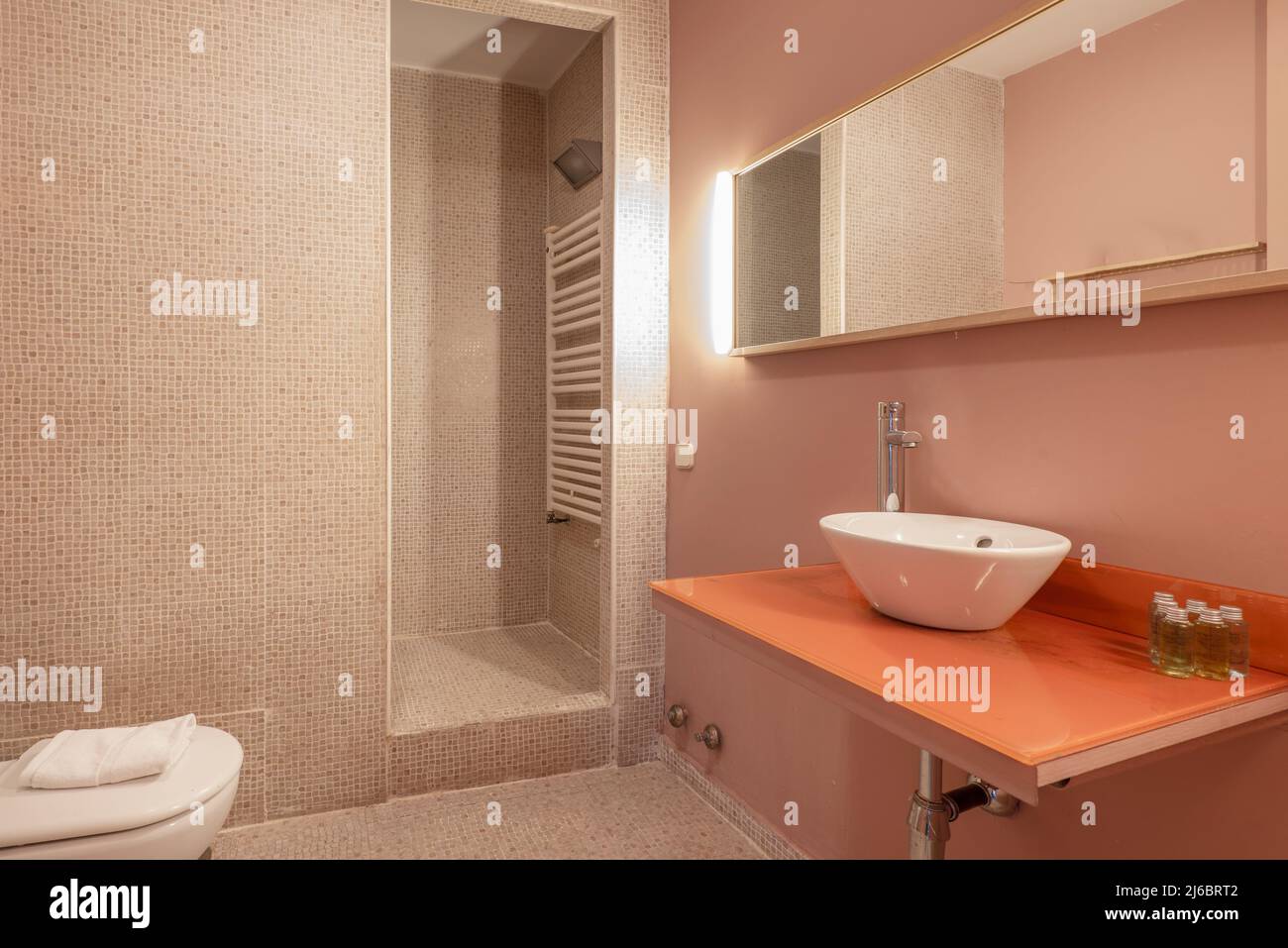 Bathroom with white porcelain sink on orange glass countertop, countertop mirror, tiled walls and walk-in shower Stock Photo