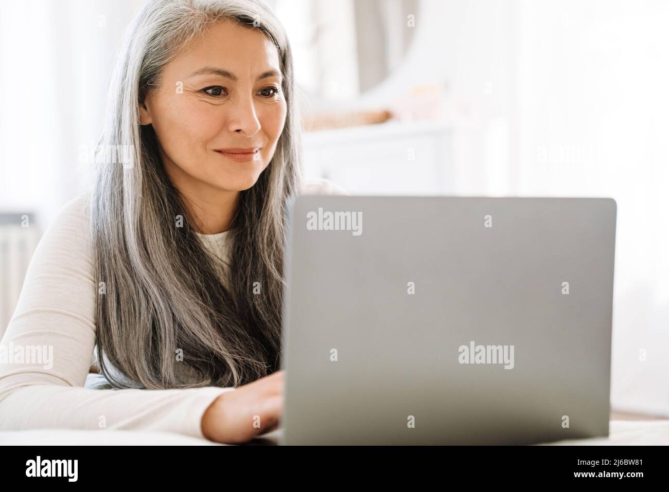 Mature asian woman with grey hair working with laptop in bedroom at ...