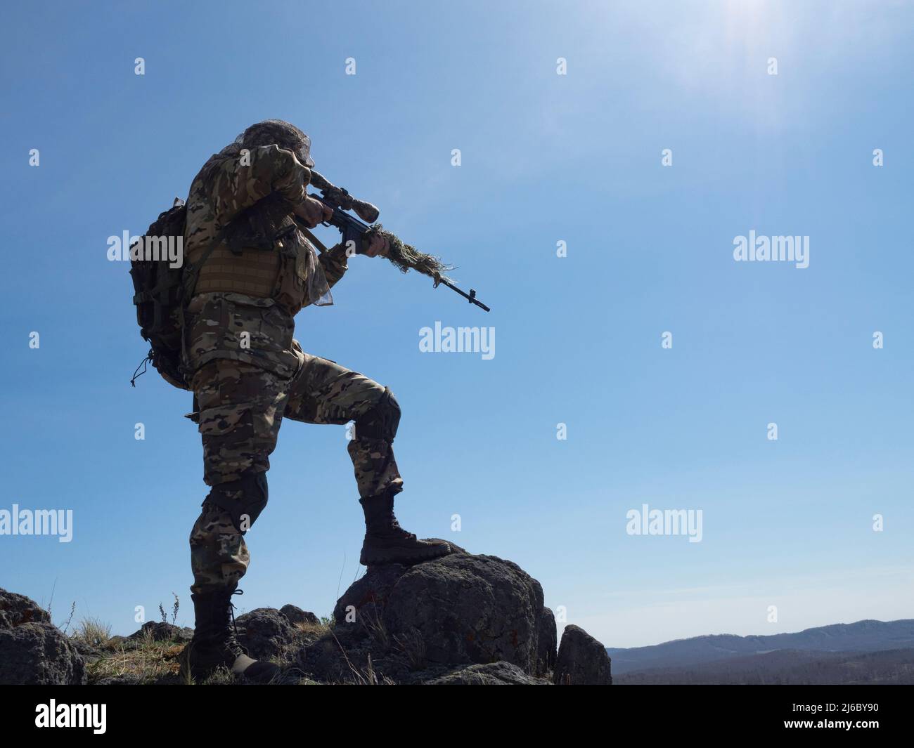 Professional special forces sniper during a special operation - he aims at the enemy. An ambush in mountains. Concept of modern military operations an Stock Photo