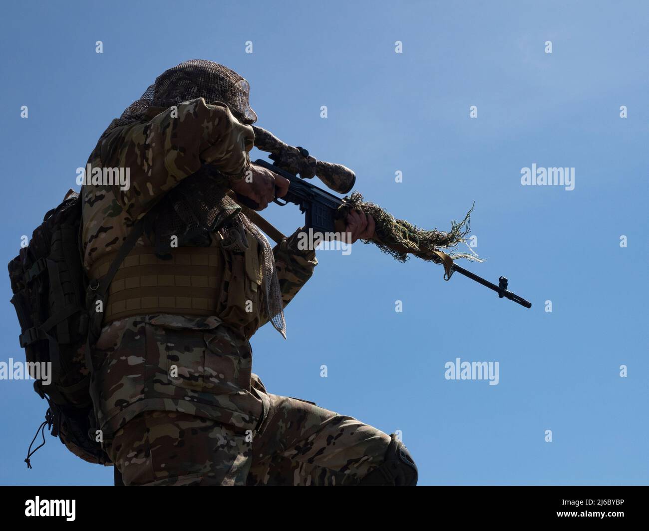 A professional special forces sniper aims at the enemy against the blue sky. Concept of modern military operations and a special operation on enemy te Stock Photo