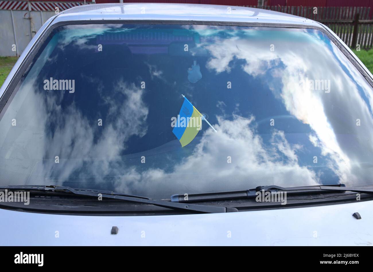 The Ukrainian flag is affixed to the windshield of a car. Reflected sky with clouds. Stock Photo
