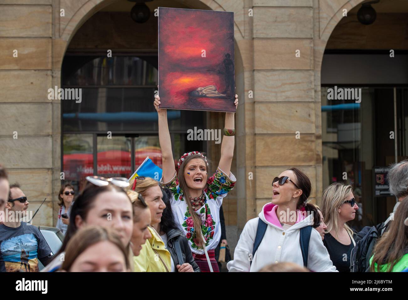 30 April 2022, Saxony, Dresden: A woman in traditional costume holds a painting of a huddled woman in the air. The counter-event against pro-Russian rally with the title: 'Solidarity with the people of Ukraine! All together against Putin's war of aggression!'also leads along Wilsdruffer Street in Dresden. Photo: Daniel Schäfer/dpa Stock Photo