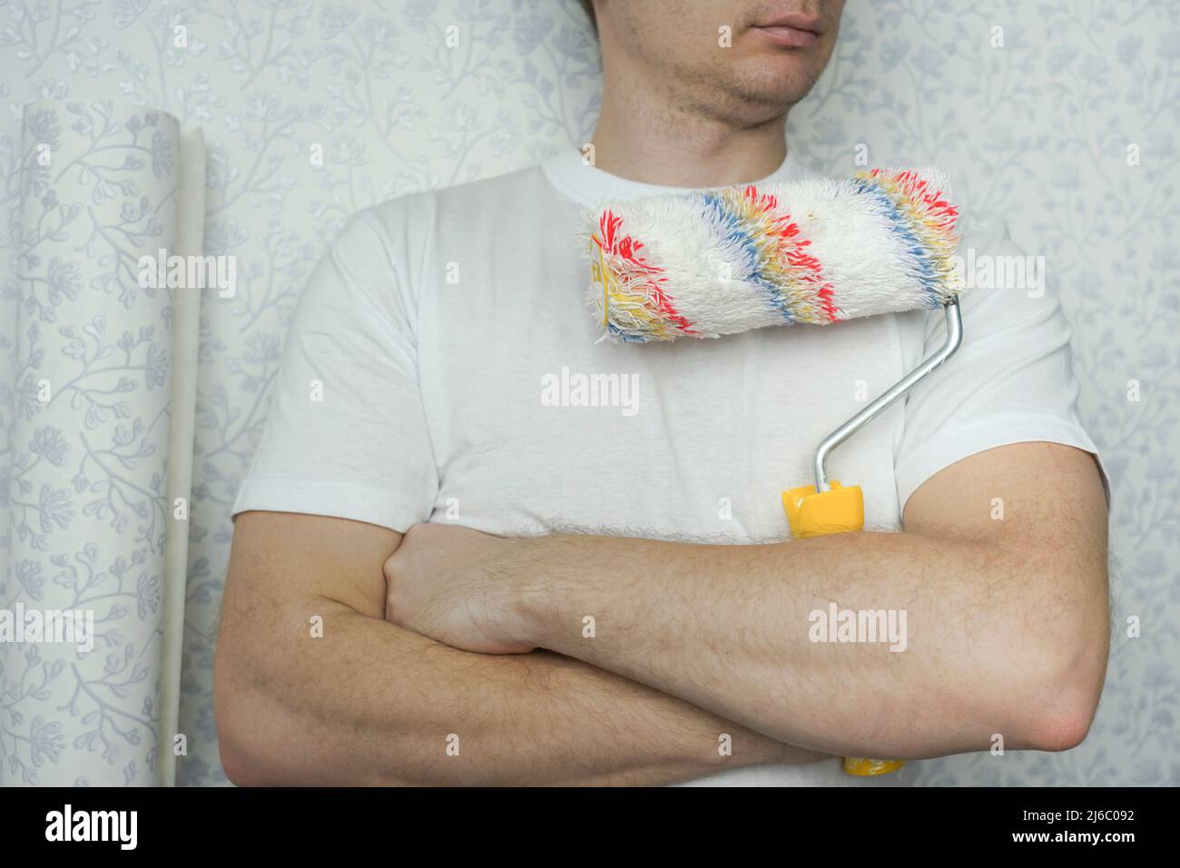 a man in a white t-shirt holds a roller with a long pile for applying glue and paint Stock Photo