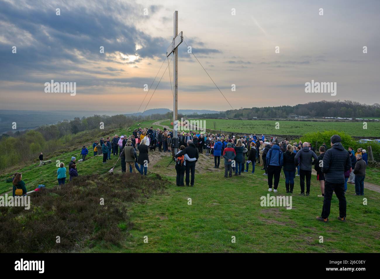 Congregation crowd gathered on hilltop for traditional Easter Sunday dawn service by high wooden cross - The Chevin, Otley, West Yorkshire England UK. Stock Photo