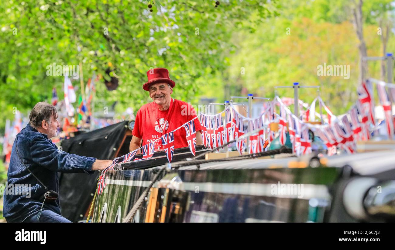 London, UK, 30th April 2022. Terry Smith, Assistant Commercial Manager of the IWA, waves from the 'Moaranwyl Phyllis', decorated in flags. Dozens of beautifully decorated narrowboats, barges and canal boats take part in the IWA Canalway Cavalcade festival which returns to London’s Little Venice for the early May Bank Holiday weekend. Organised by the Inland Waterways Association (IWA), it celebrates boat life with a boat pageant, as well as music, stalls and family entertainment along the Grand Union Canal. Stock Photo