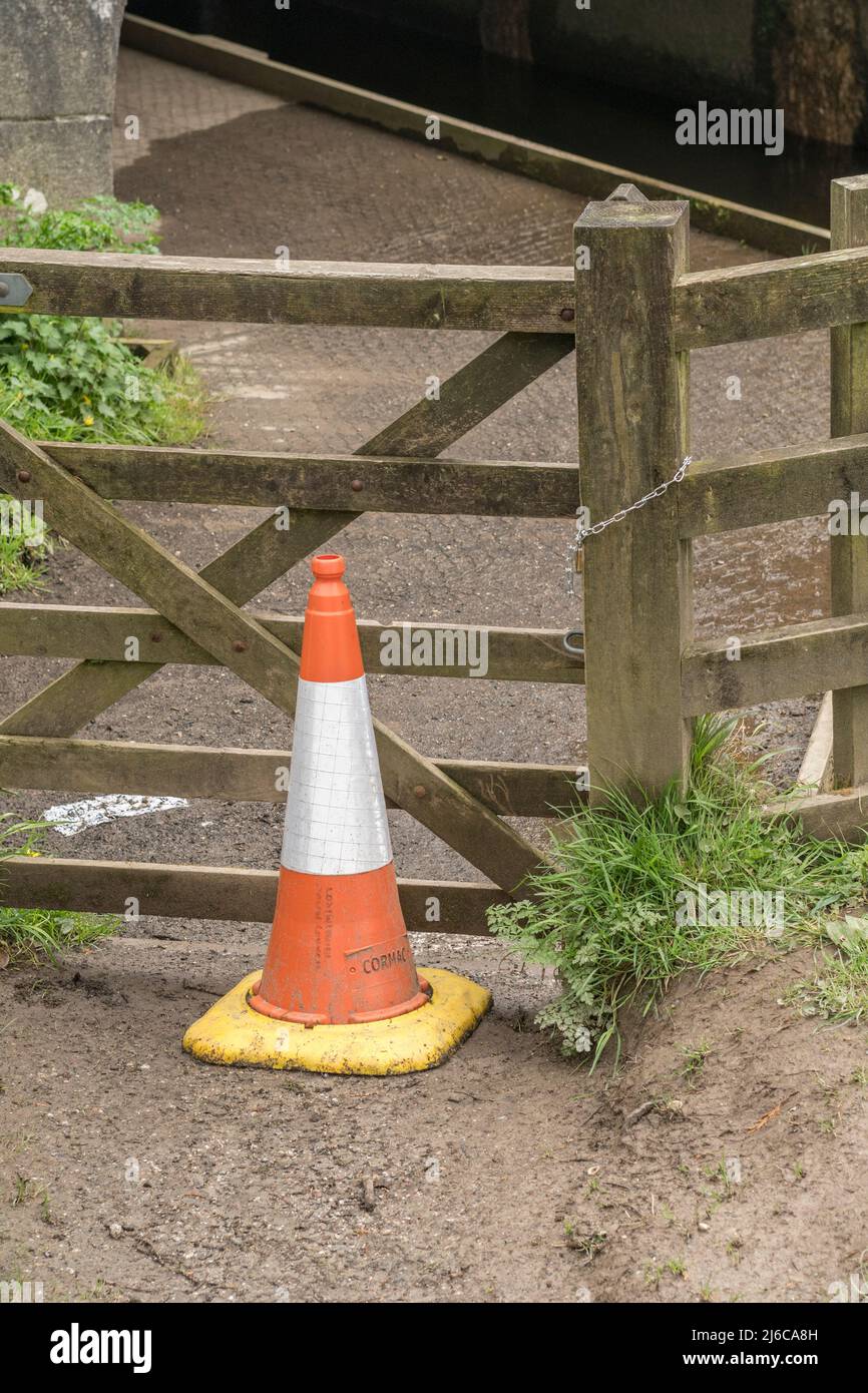 Orange and white road cone used to warn pedestrians / walkers not to use a footpath running alongside the River Fowey. For safety, danger warning. Stock Photo