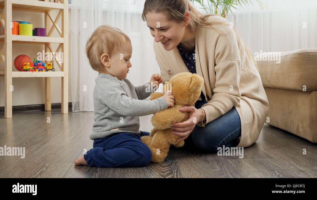 Happy smiling mother teaching her baby son and playing with teddy bear Stock Photo