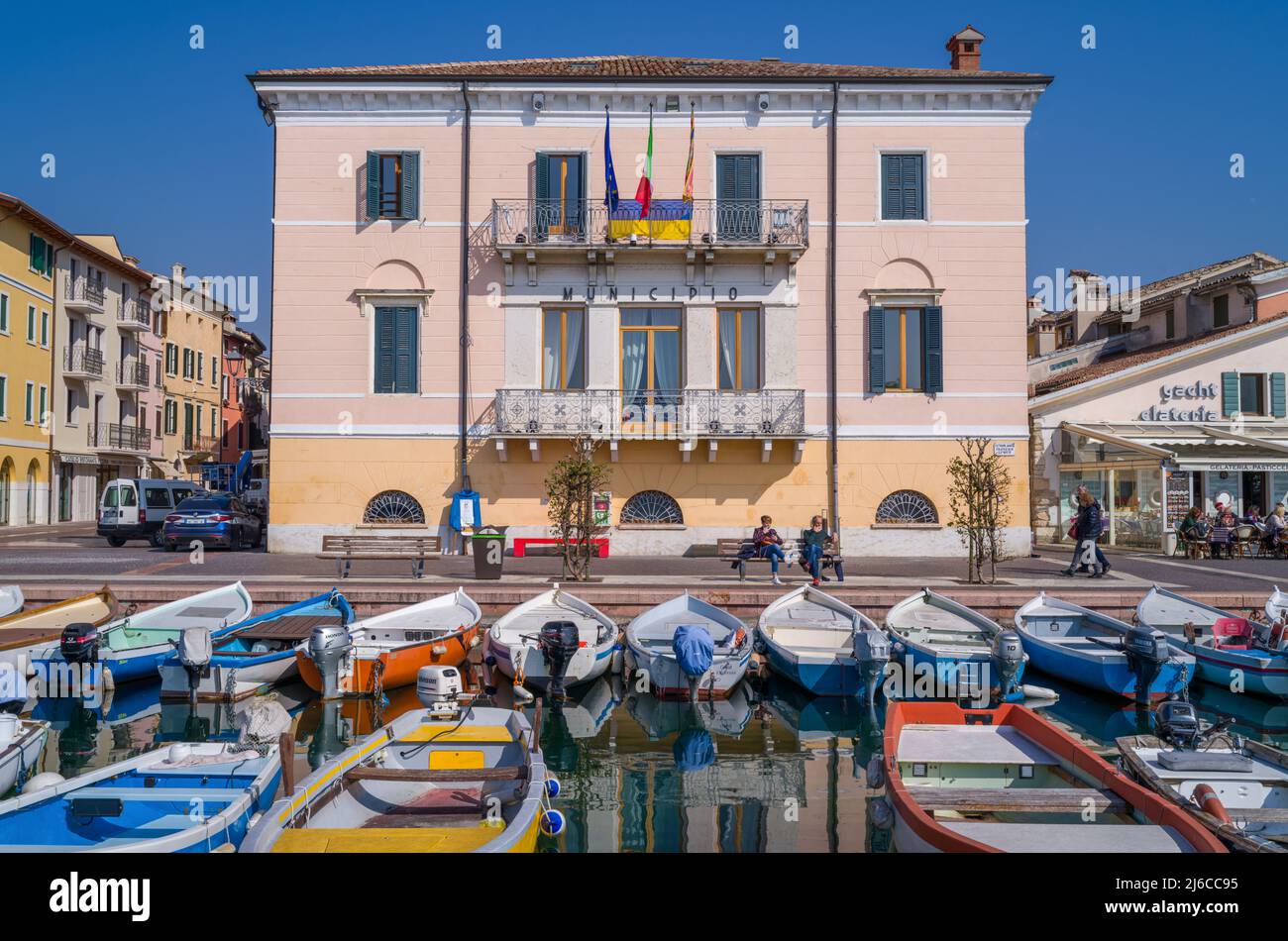 Bardolino, Italy - March 10, 2022:  Boats in the old harbor with the city Hall and restaurants in the backgraund Stock Photo