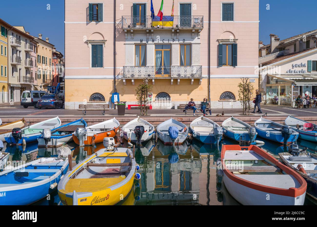 Bardolino, Italy - March 10, 2022:  Boats in the old harbor with the city Hall and restaurants in the backgraund Stock Photo