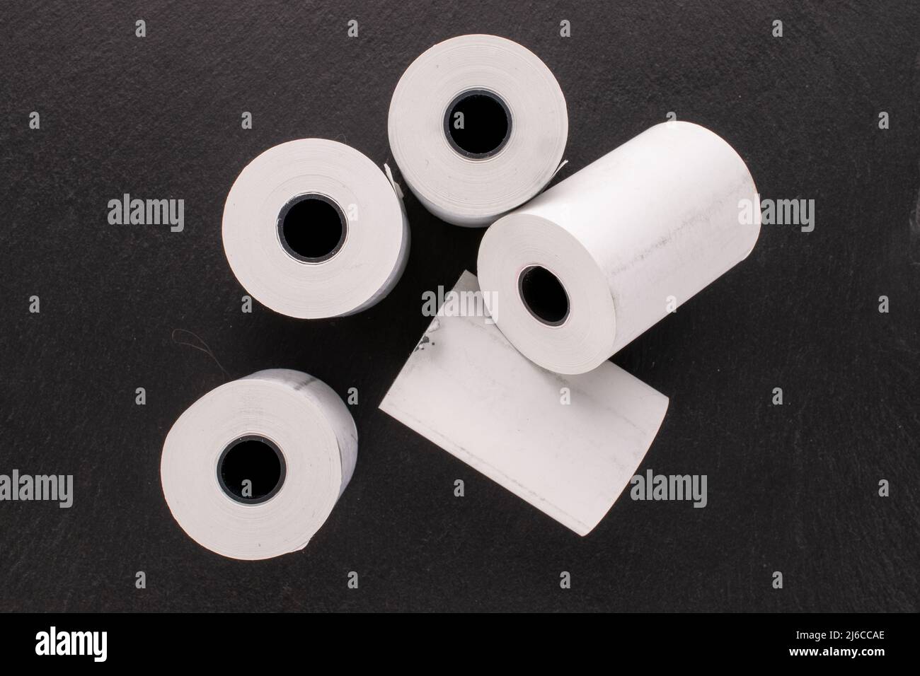 Several rolls of paper tape for a cash register on a slate stone, macro, top view. Stock Photo