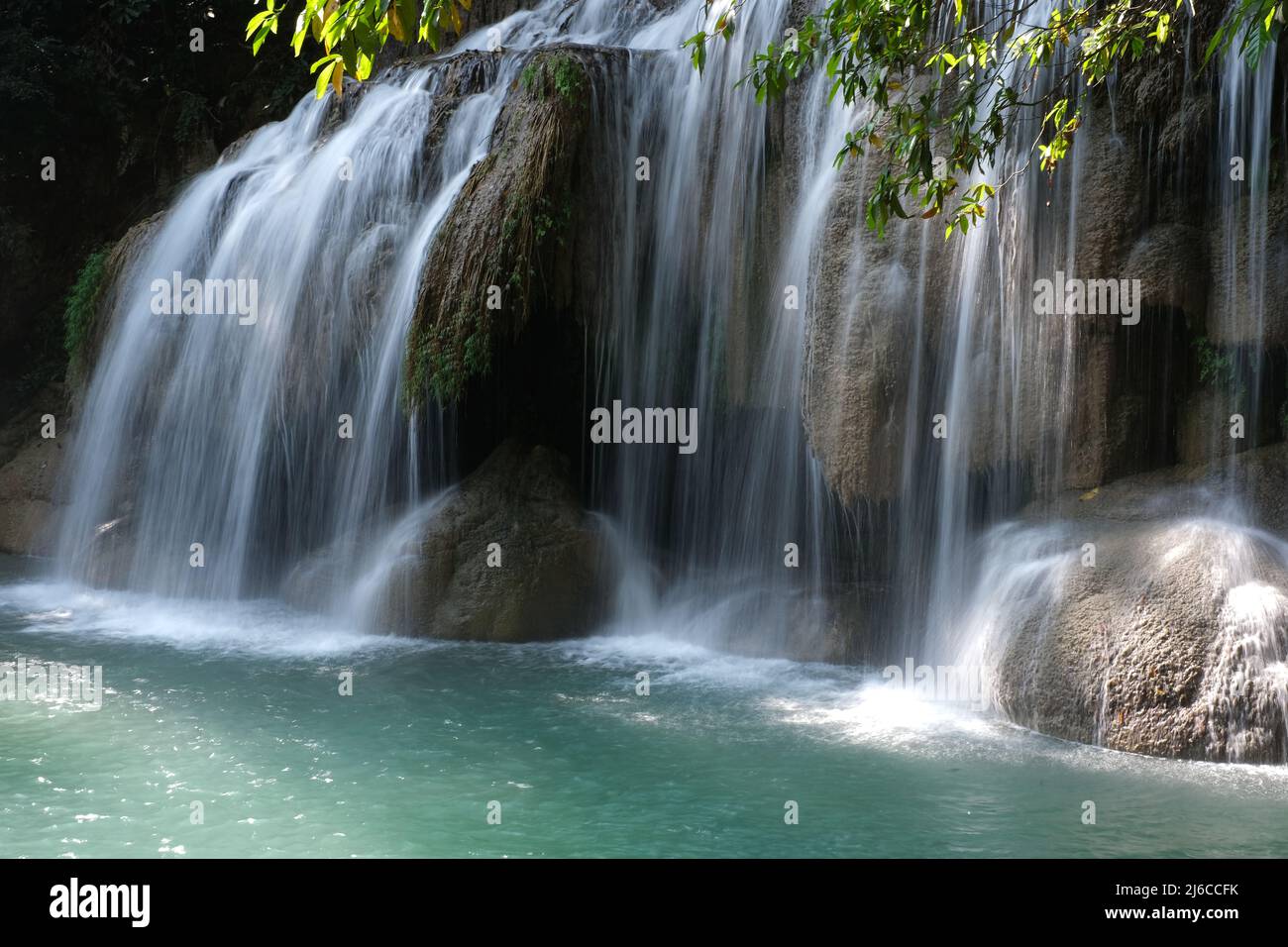 Waterfall on a clean emerald river covers a small cave, at one of the cascades of Erawan Falls in Thailand Stock Photo
