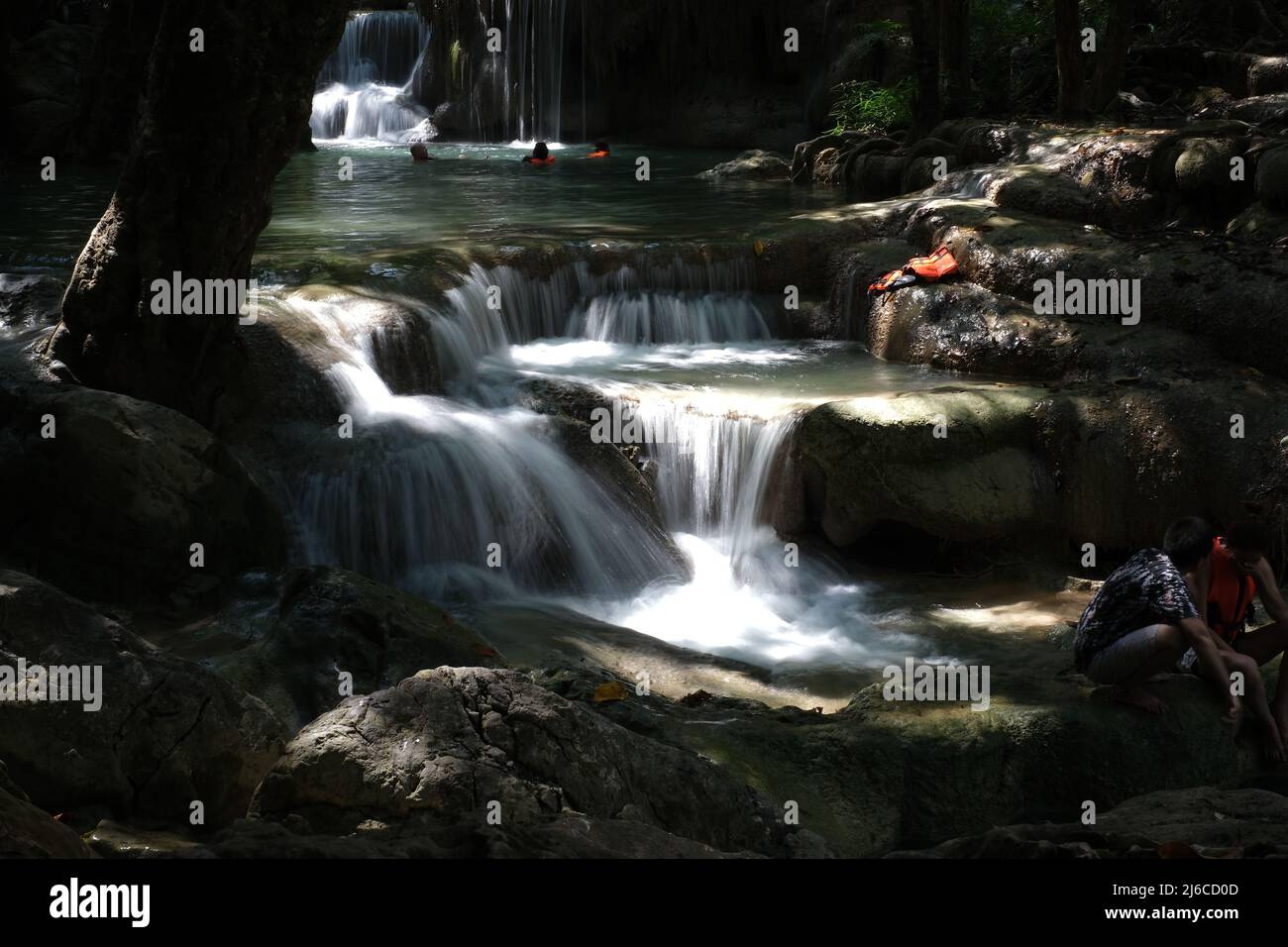 Cascade of waterfalls and relaxing people on a mountain river at Erawan Falls in Thailand Stock Photo