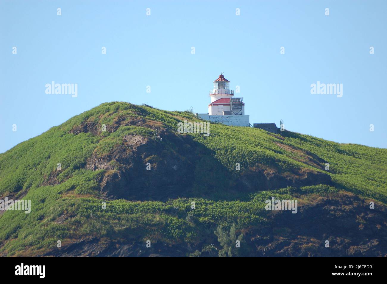 lighthouse on top of a rocky cliff overgrown with grass Stock Photo