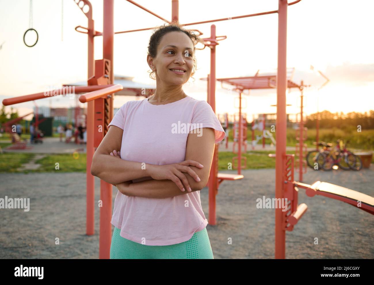 Confident portrait of a pleasant middle aged multiethnic woman, athlete, sportswoman in activewear posing with crossed arms against crossbar in the sp Stock Photo