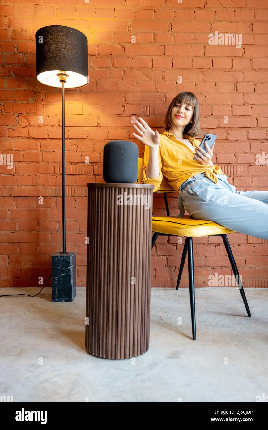 Woman with smart speaker and phone at home Stock Photo