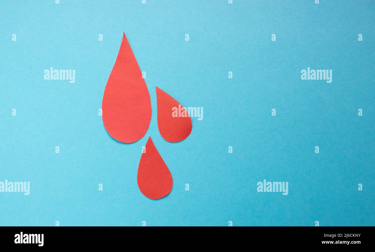 The concept of the World Blood Donor and Hemophilia Day. Red paper drops of blood on a blue background. Stock Photo