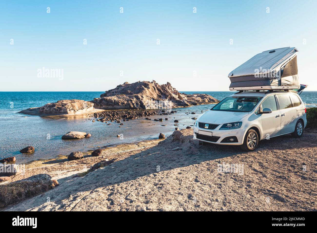 Vanlife camping at the sea - white van with roof tent on the shore of a  rocky